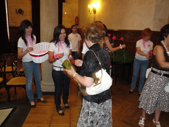 Alumnos recibiendo a los asistentes al acto y entregando claveles y lazos rosas.